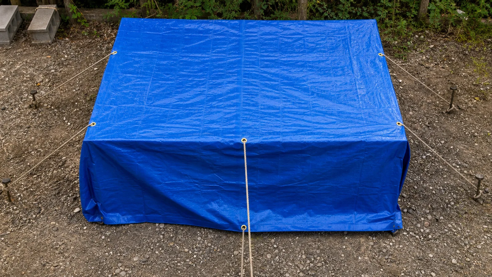 Blue tarp tensioned at the corners with rope through metal grommets to outdoor anchor points